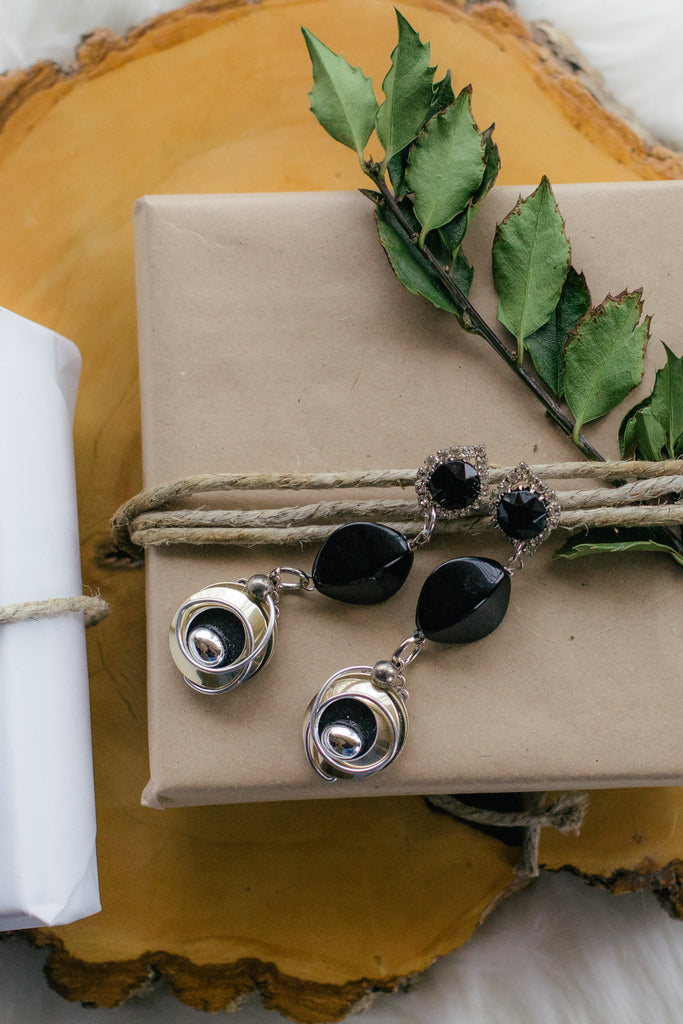 black and silver vintage earrings on top of kraft brown gift wrapped paper with holly on wood
